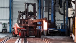 Das Gerät hat ein spezielles Anbaugerät für den Transport zum nächsten Bearbeitungsschritt. Das Gerät transportiert ein glühendes Eisen über das Gelände.