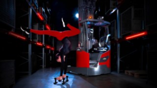 Ein Akrobat, der neben dem Linde-MH-Schubmaststapler Ri16 in einem Lagerhaus einen Handstand macht.