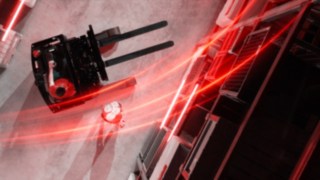 Der Linde-MH-Schubmaststapler Ri16 aus der Vogelperspektive mit roten Lichtspuren, daneben eine Person, die einen Handstand macht.