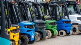 Mietstaplerflotte seitlich mit Heckansicht der Stapler, Aufreihung hintereinader verschiedene Staplermodelle, in unterschiedlichen Lackierungen. 