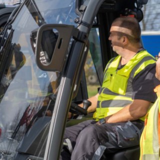 Zwei Mitarbeiter bei der Einweisung im und am Gabelstapler, einer sitzt im Stapler