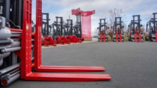Video der Übergabe der Linde X Gabelstaplerflotte an Cabka GmbH & Co. KG Gabelstapler mit abgesetzten Gabelzinken links im Vordergrund, im Hintergrund die Staplerflotte aufgereiht mit verschiedenen Anbaugeräten, in der Mitte die Firmenfahne von CABKA