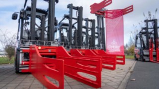 Drei Linde Gabelstapler mit Ballenklammer in rot als Anbaugerät in Reihe gestellt, rechts eine Fahne der Firma CABKA hängend am Anbaugerät angebracht