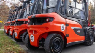 Die Linde X30 Gabelstapler aufgereiht auf einem Parkplatz, nach hinten in Heckansicht, vorn in groß zu sehen dann werden die Stapler immer kleiner, links ist Wiese