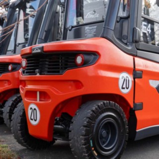 Die Linde X30 Gabelstapler aufgereiht auf einem Parkplatz, nach hinten in Heckansicht, vorn in groß zu sehen dann werden die Stapler immer kleiner, links ist Wiese