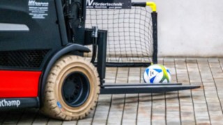 Gabelstapler führt mit Gabelzinken Fußball in ein Fußballtor