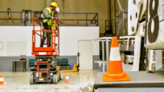 Hubarabeitsbühnenbediener in einer Scherenbühne beim üben in einer Halle