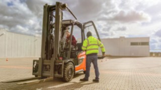 Staplerfahrer im Linde Gabelstapler, Fahrschultrainer hat Tür vom Stapler geöffnet um einzuweisen. 