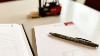 Block mit Stift von MV Födertechnik auf einem Tisch liegend. Im Hintergrund ein Staplermodell.