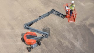 Skyjack SJ46 AJ Gelenkteleskopbühne mit Bediener im Korb auf sandigen Untergrund, sicht von der Volgelperspektive auf die Bühne