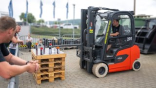 Mini-Fässer Parcours Action StaplerCup Qualifier  Zuschauer links am Gitter, rechts der Stapler im Pacours beim fahren
