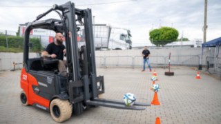 Staplerfahrer hat mit dem Stapler einen Fußball von einem Pilonen mit den Gabelzinken aufgenommen