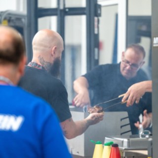 Staplerfahrer im Vordergrund links, im Hintergrund der Bratwurstrost 