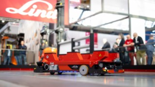 Linde C-Matic Automatisierungsfahrzeug in Bewegung auf einem Messestand im Hintergrund das Linde Logo